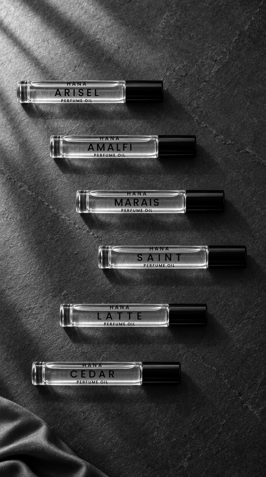 Six HANA perfume oils arranged on a dark stone surface